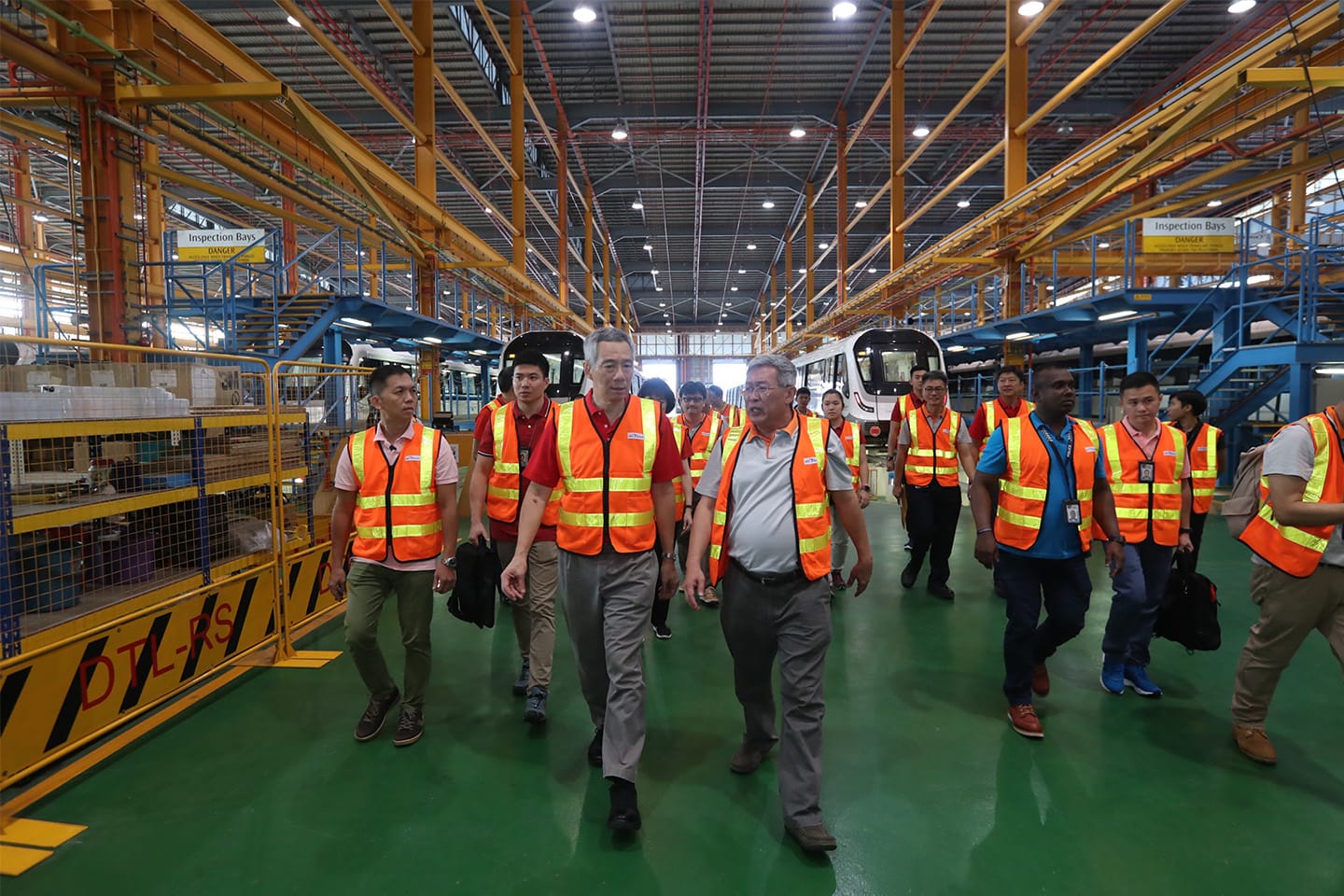Group of people in safety vests walking through a train manufacturing warehouse.